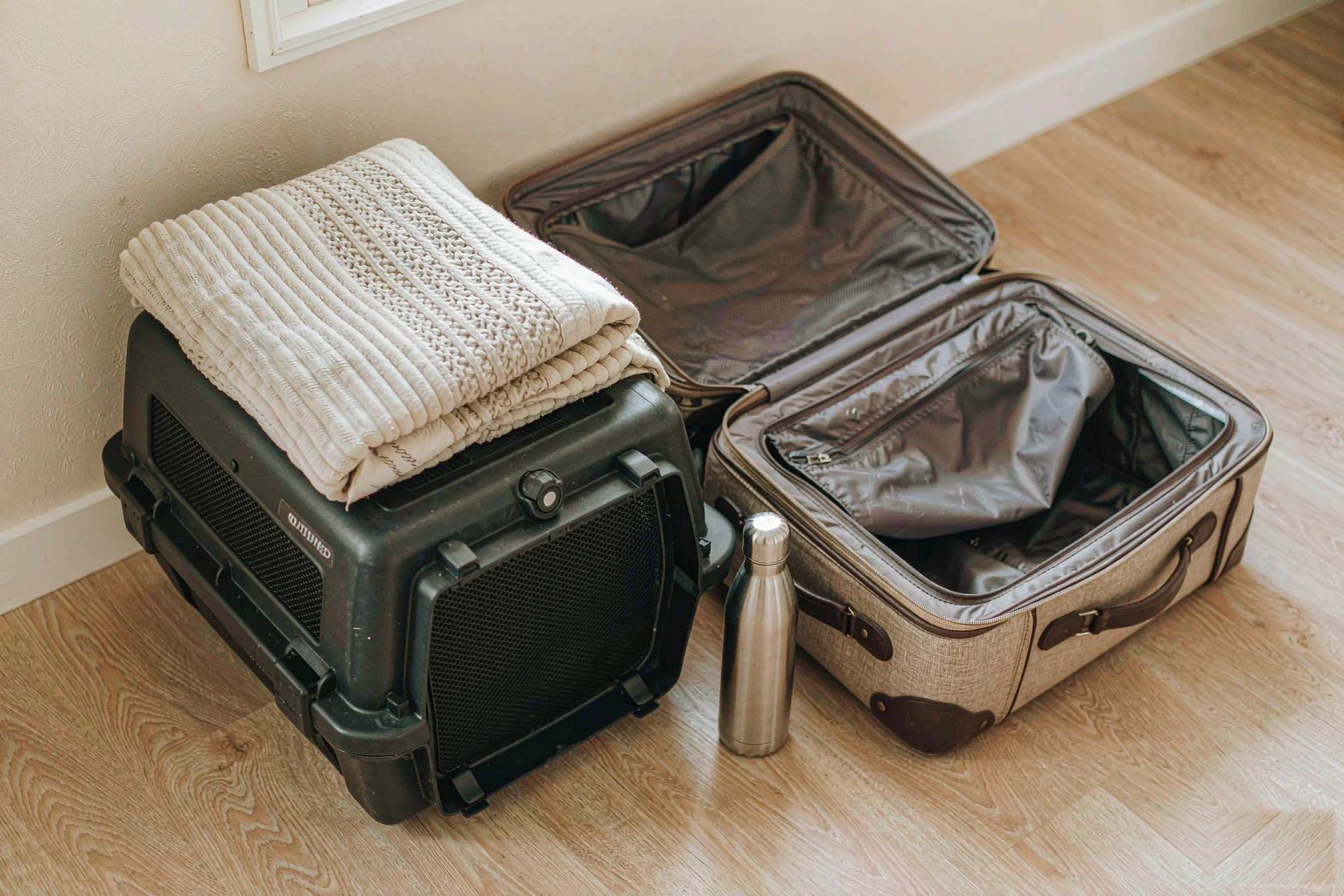 Packing a hard-shell pet crate and steel bottle beside a suitcase